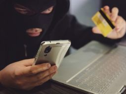 Male hacker in a robber mask uses phone, credit card and laptop in some fraudulent scheme. Cyber thief stole the personal data and credit card information. Hacker uses malware to steal user&#039;s money